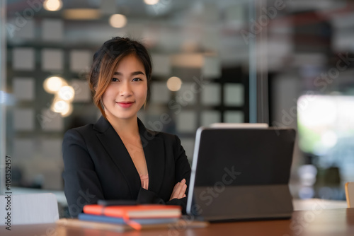 Portrait of a female entrepreneur looking into the camera while working with a computer in an office room. © Songsak C