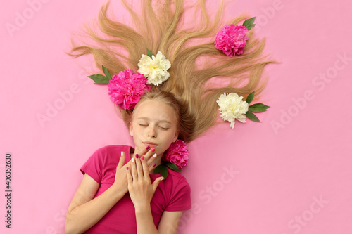 A girl with peonies, beautiful blonde hair and a colorful children's manicure on a pink background.Fashion nail art and hairstyle.