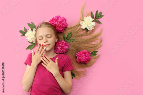 Fototapeta Naklejka Na Ścianę i Meble -  A girl with peonies, beautiful blonde hair and a colorful children's manicure on a pink background.Fashion nail art and hairstyle.
