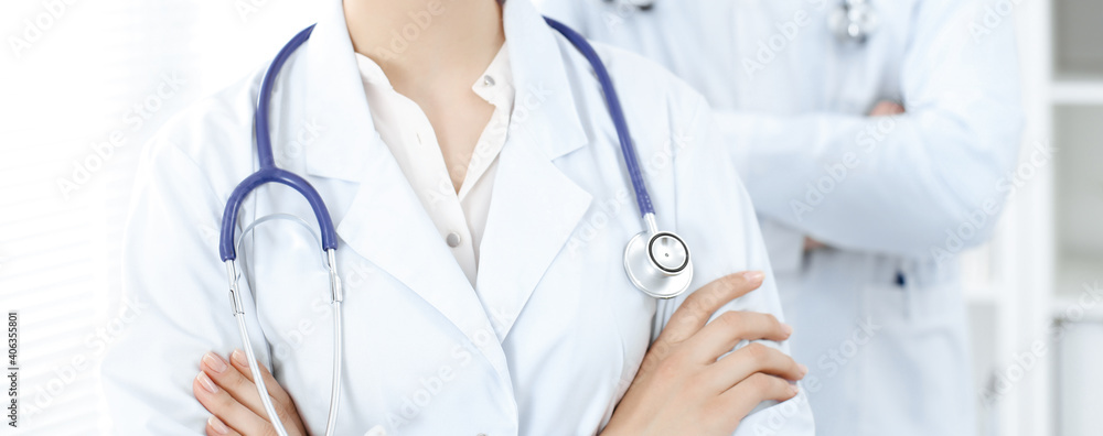 Unknown woman-doctor standing straight with arms crossed in clinic, close-up. Medical team ready to stop coronavirus pandemic. Medicine concept Unknown woman-doctor standing straight with arms crossed in clinic, close-up. Medical team ready to stop coronavirus pandemic. Medicine concept