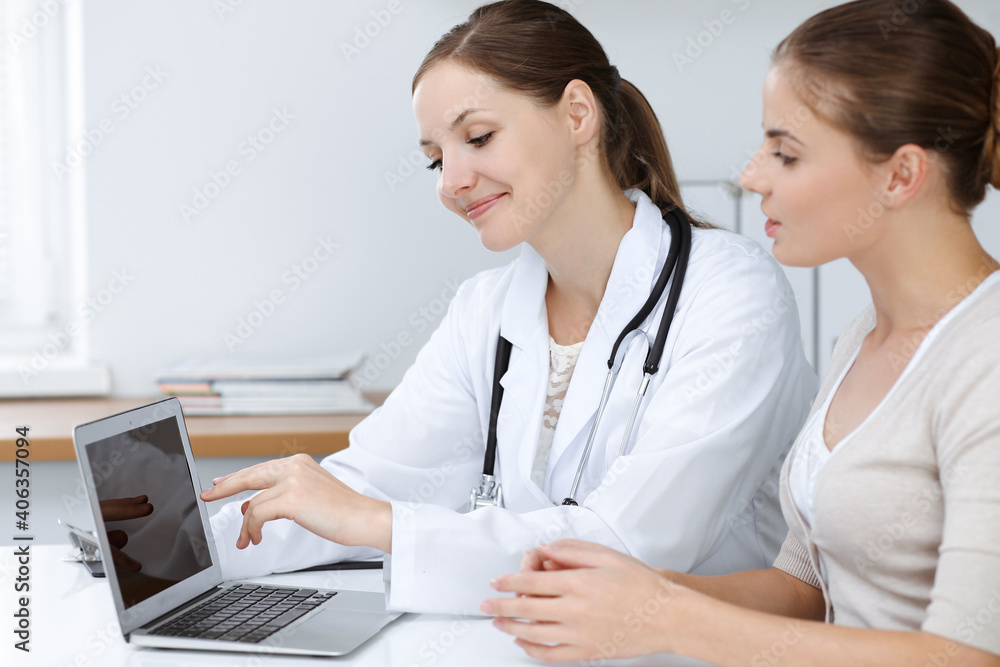 Doctor and patient are sitting and discussing health examination results while using laptop computer. Health care, medicine and good news concepts Doctor and patient are sitting and discussing health examination results while using laptop computer. Health care, medicine and good news concepts