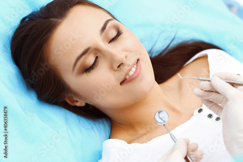 Young female patient visiting dentist office.Beautiful woman with healthy straight white teeth sitting at dental chair with open mouth during oral checkup while doctor working at teeth