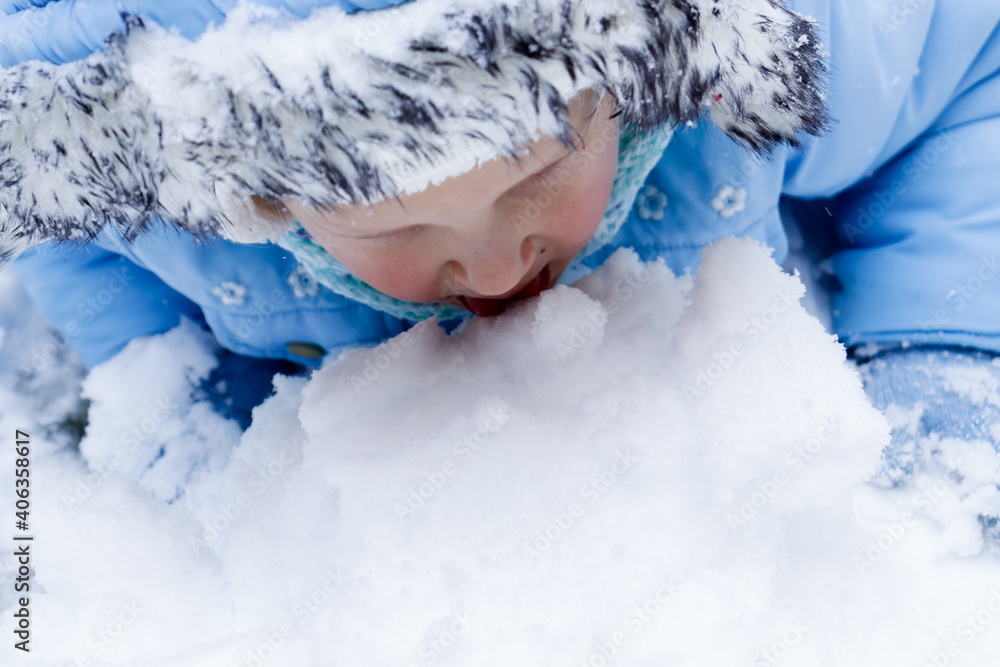 The baby is playing with the snow. Blue mittens and a blue jacket in the snow. The child lies and eats snow. The baby is playing with the snow. Blue mittens and a blue jacket in the snow. The child lies and eats snow.
