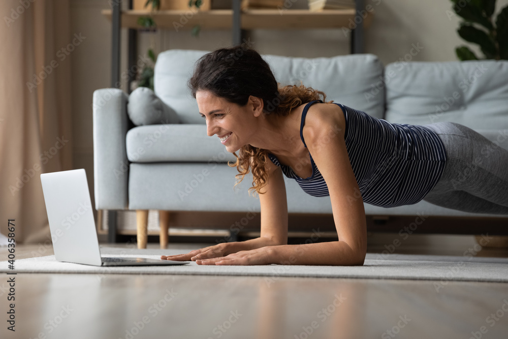 Smiling young sporty woman look at laptop screen practice yoga or stretching using webcam class on computer. Happy active millennial female do morning gymnastics train online on computer from home. Smiling young sporty woman look at laptop screen practice yoga or stretching using webcam class on computer. Happy active millennial female do morning gymnastics train online on computer from home.