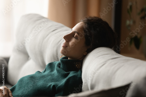 Calm young woman sit rest on cozy sofa at home sleep or take nap doing lazy weekend indoors. Millennial female relax on couch in living room daydream relive negative emotions. Stress free concept. photo
