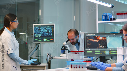 Man research scientist looking at samples under microscope while nurse writes informations on pc in modern equipped laboratory. Doctors working with various bacteria, tissue and blood tests