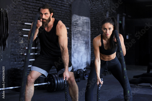 Athletic young couple with battle rope doing exercise in functional training fitness gym.