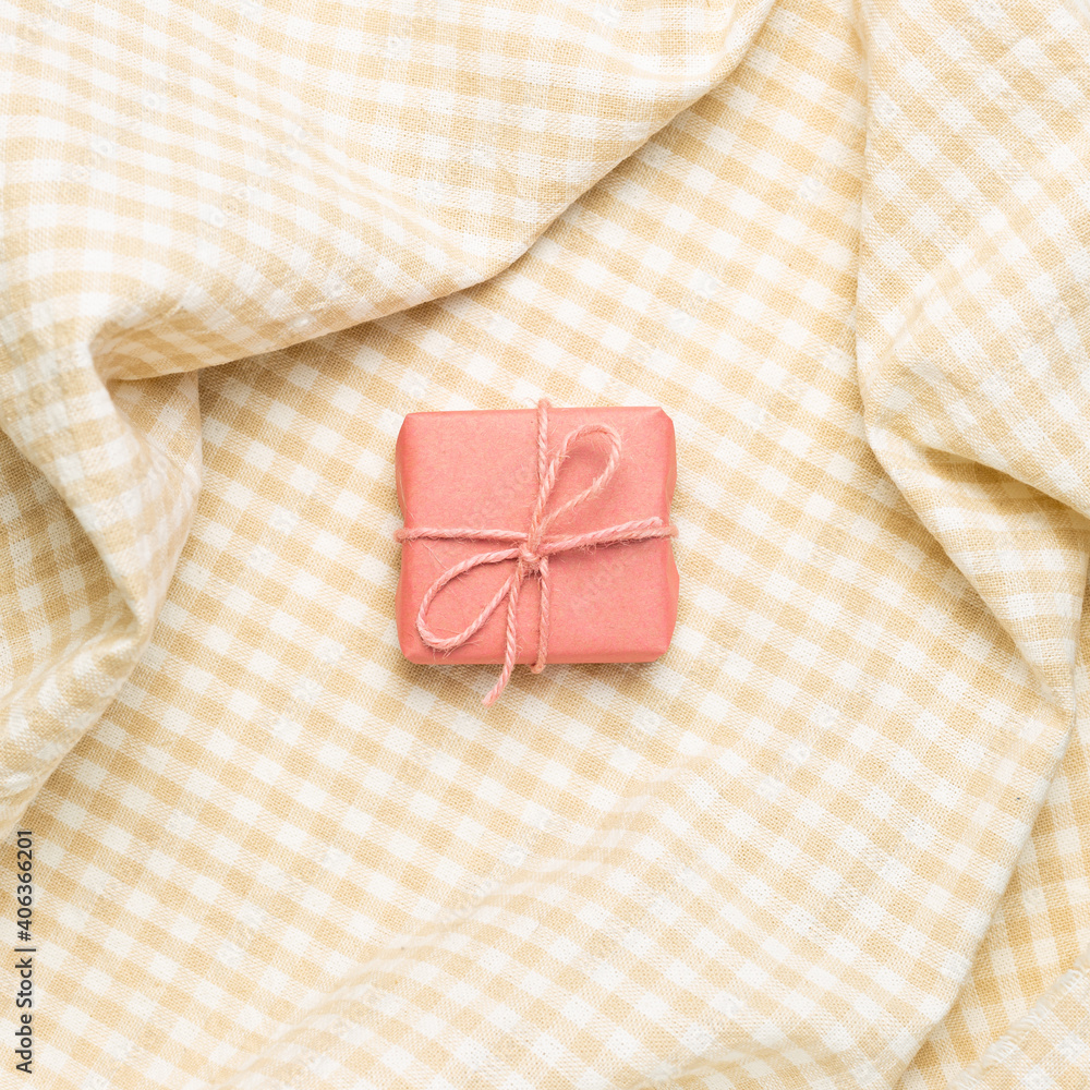 Pink gift box on crumpled beige check pattern fabric background. top view
