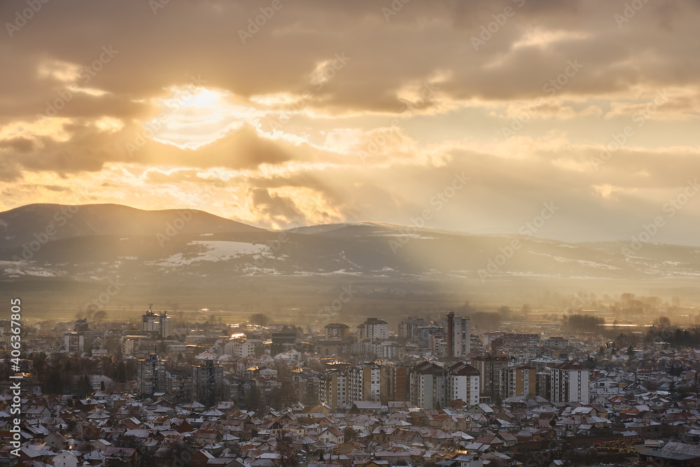 Golden hour view of Pirot cityscape on a cold, frosty, winter day with snow on the houses and distant horizon mountains under colorful sky