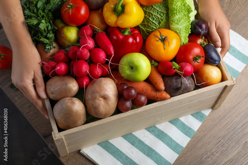 Fototapeta Naklejka Na Ścianę i Meble -  Farmer with crate full of different vegetables and fruits at wooden table, closeup. Harvesting time