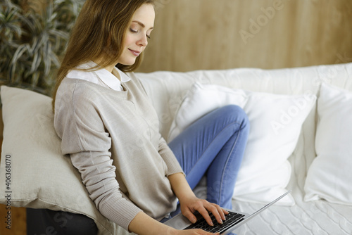 Business woman working on laptop computer sitting indoors during Covid-19 quarantine in cozy living room. Stay at home concept during Coronavirus pandemic