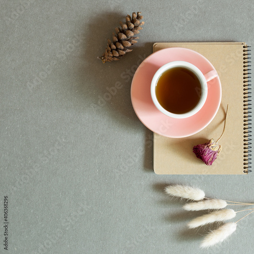 Cup of black tea on notebook with dry plant on gray background. top view, copy space