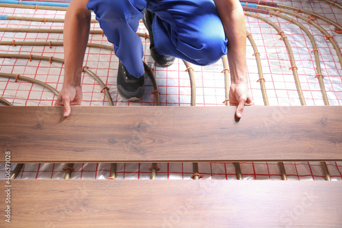 Worker installing new wooden laminate over underfloor heating system, closeup