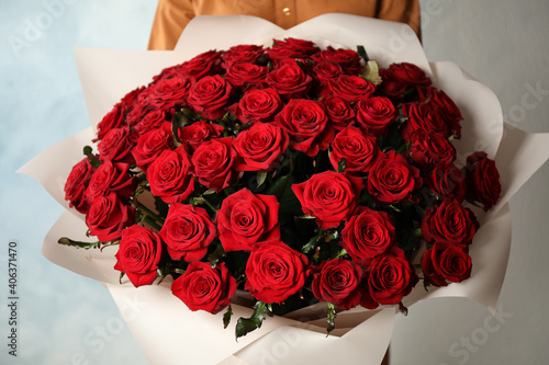 Fototapeta Naklejka Na Ścianę i Meble -  Woman holding luxury bouquet of fresh red roses on light background, closeup