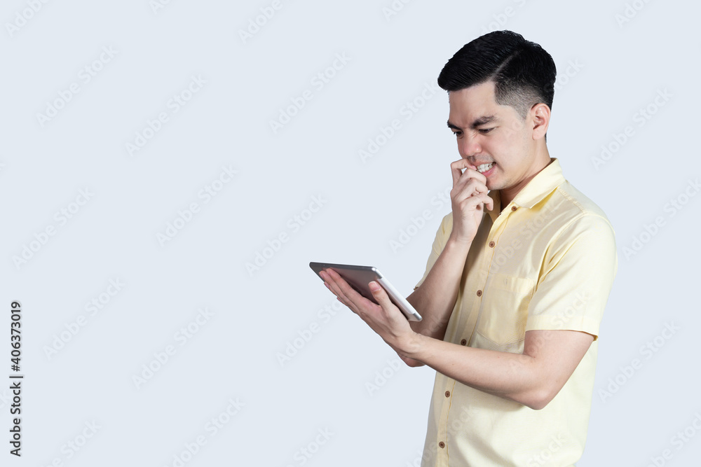 Terrible headache. portrait handsome young asian man wearing a yellow shirt holding smart phone or tablet feeling stressful isolated on white background. Businessman concept. Asia people. Terrible headache. portrait handsome young asian man wearing a yellow shirt holding smart phone or tablet feeling stressful isolated on white background. Businessman concept. Asia people.