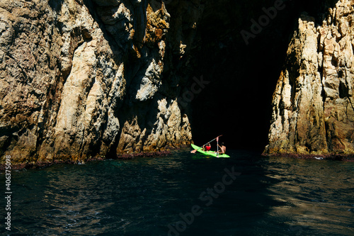 Selective focus - father and son rowing in a canoe to enter a natural cave in the Mediterranean Sea