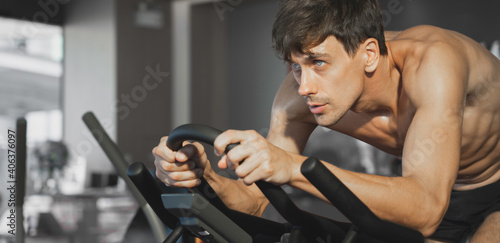Handsome caucasian athlete muscular male exercise on spinning bike at fitness gym, Banner with copy space