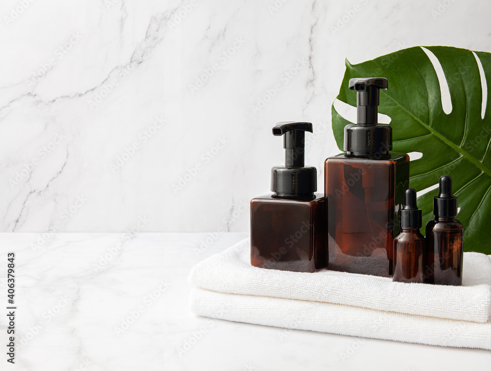 Amber glass cosmetic bottles set with towel and monstera leaf on marble background. Copy space Amber glass cosmetic bottles set with towel and monstera leaf on marble background. Copy space