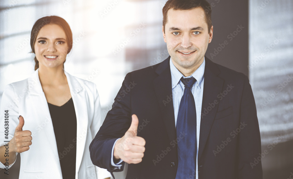 Smiling businesspeople are happy with a good result of their teamwork, standing with thumbs up in a sunny modern office. Concept of business success Smiling businesspeople are happy with a good result of their teamwork, standing with thumbs up in a sunny modern office. Concept of business success