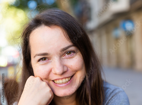 Closeup portrait of cheerful brunette outdoors on blurred summer city street background