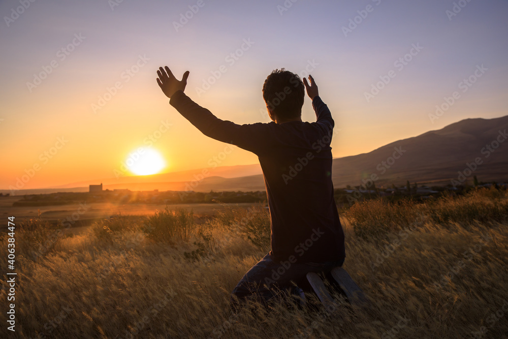 man with hands raised in the sunset