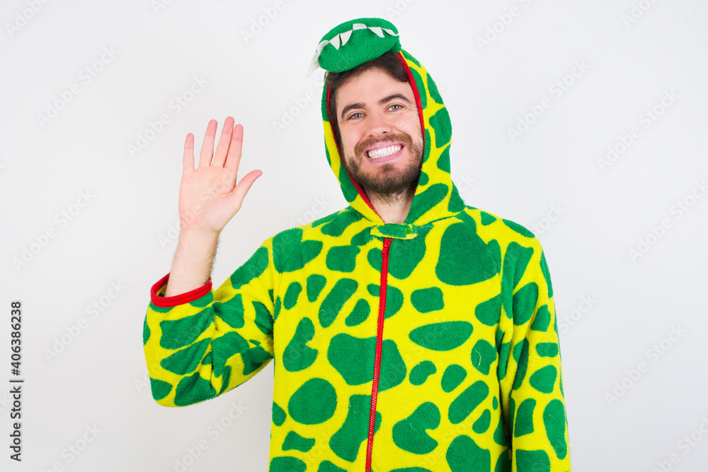 Fototapeta premium Young caucasian man wearing a pajama standing against white background Waiving saying hello happy and smiling, friendly welcome gesture.
