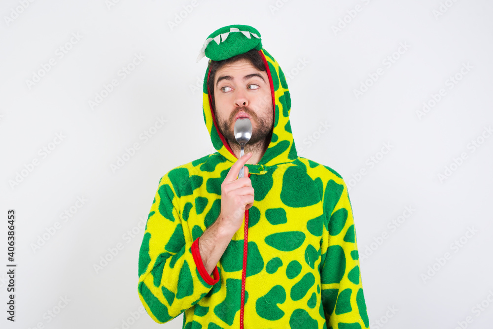 Very hungry Young caucasian man wearing a pajama standing against white background holding spoon into mouth dream of tasty meal Very hungry Young caucasian man wearing a pajama standing against white background holding spoon into mouth dream of tasty meal