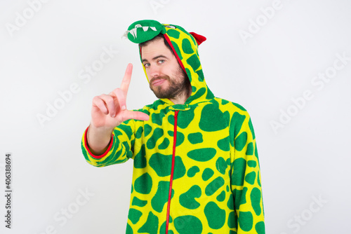 Young caucasian man wearing a pajama standing against white background making fun of people with fingers on forehead doing loser gesture mocking and insulting.