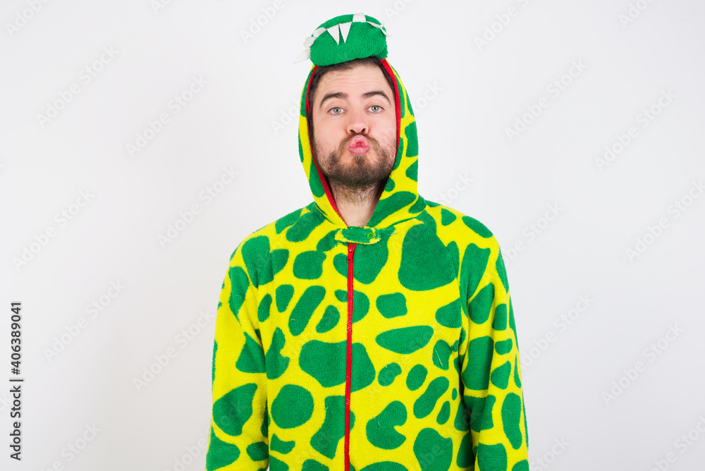 Fototapeta premium Shot of pleasant looking Young caucasian man wearing a pajama standing against white background, pouts lips, looks at camera, Human facial expressions