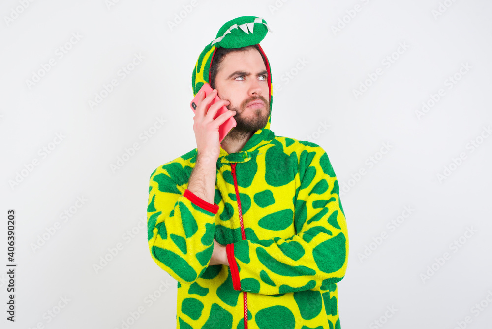 Fototapeta premium Sad Young caucasian man wearing a pajama standing against white background talking on smartphone. Communication concept.