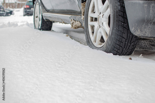 Closeup of the car tire on winter road covered with snow. Snowflakes are on the rubber wheel.