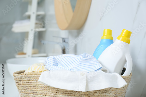 Bottles of detergent and children s clothes in wicker basket indoors  closeup