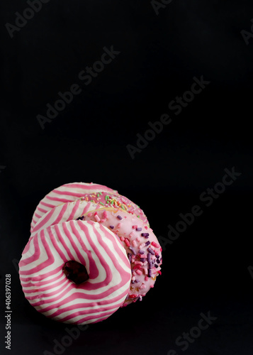 Donuts with pink icing on black background with copy space and flat lay