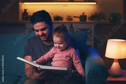 happy father is reading a fairytale book to toddler baby girl at home. bedtime story photo