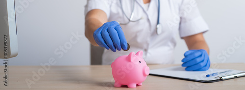 A faceless female doctor puts a coin in a piggy bank. Widescreen