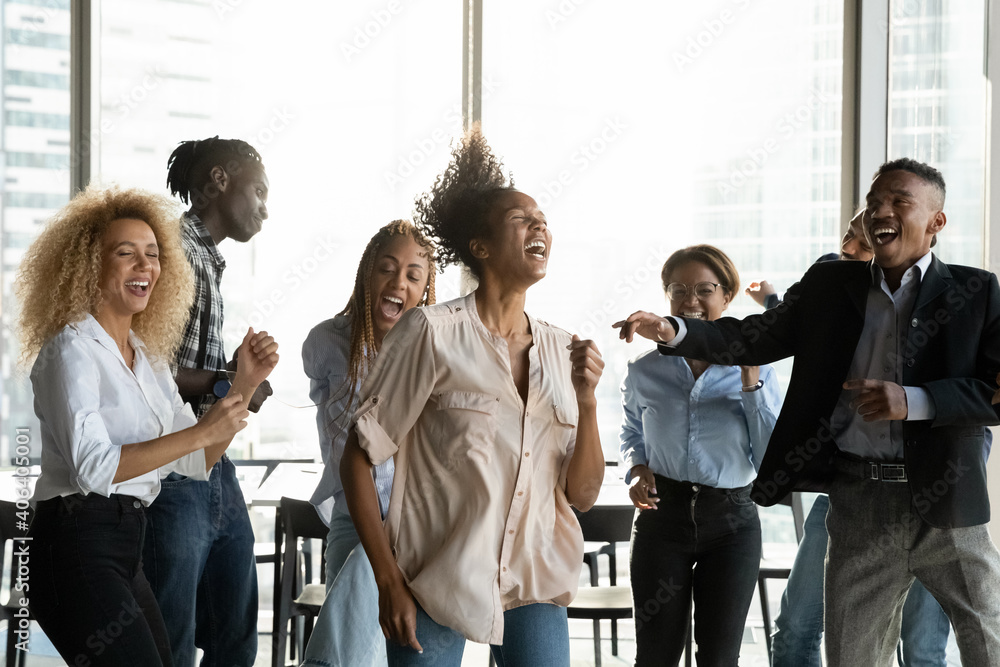 Naklejka premium Overjoyed diverse multiracial colleagues have fun dancing together at office party. Happy multiethnic employees feel excited joyful celebrate Friday or weekend at workplace. Celebration concept.