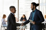 Smiling African American boss or CEO handshake excited ethnic male employee congratulate with promotion. Happy multiethnic businessmen shake hands close deal or greet in office. Acquaintance concept.