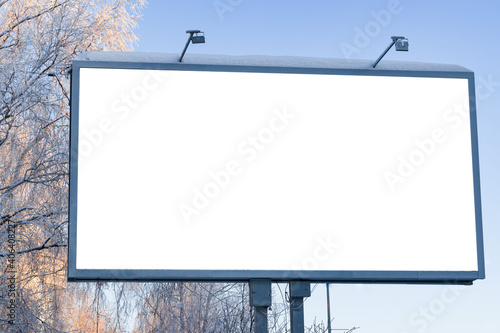 Billboard on the street in the city with an empty white space for text on a background of trees in frost, snow, blue sky, beautiful winter background, mock up