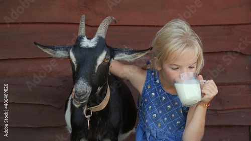 Fotografia The girl drinks goat milk from a mug and hugs her beloved goat.