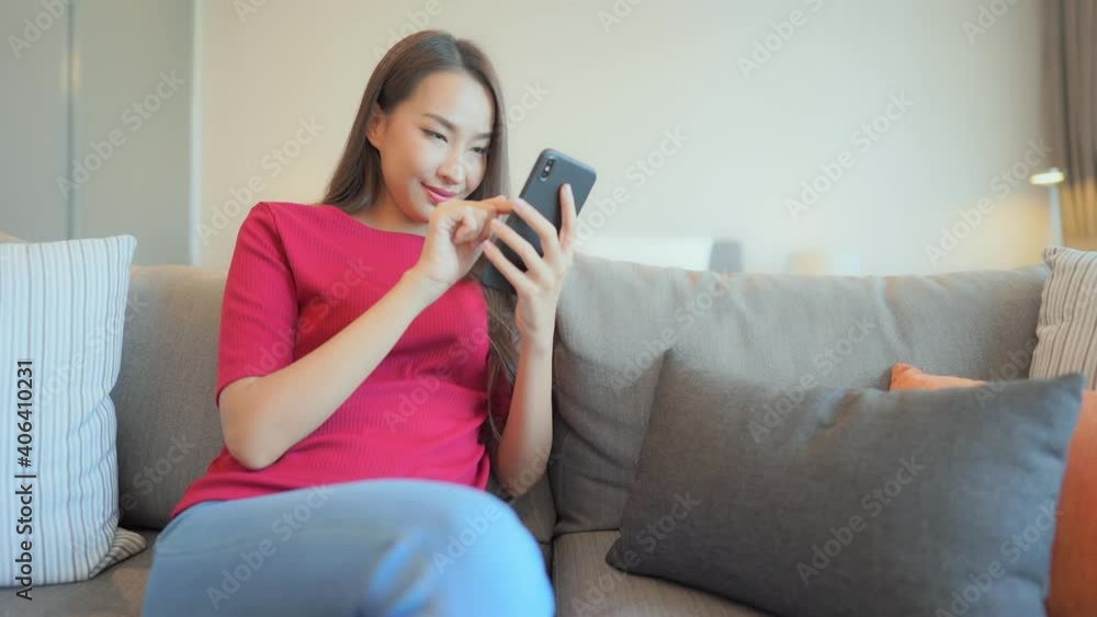 Happy Asian Female Texting on Mobile Phone While Sitting on Sofa in Family Home. Static Full Frame, Social Networking Concept Happy Asian Female Texting on Mobile Phone While Sitting on Sofa in Family Home. Static Full Frame, Social Networking Concept