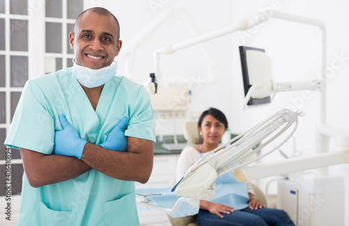 Portrait of successful professional latin american dentist standing in blue uniform in modern medical dental office