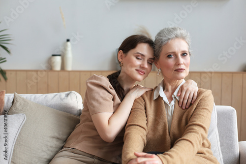 Portrait of old mother and mature daughter hugging at home. Happy senior mom and adult daughter embracing with love on sofa.