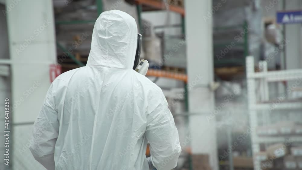 Worker in protective suit spraying sanitizer in stock room Worker in protective suit spraying sanitizer in stock room