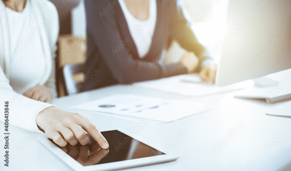 Businesswoman pointing at tablet computer screen while giving presentation to her female colleague. Group of business people working at the desk in office. Teamwork concept Businesswoman pointing at tablet computer screen while giving presentation to her female colleague. Group of business people working at the desk in office. Teamwork concept