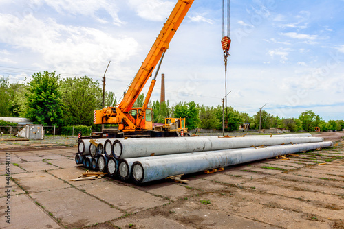 Unloading of concrete high-voltage poles at the construction site using a lifting crane