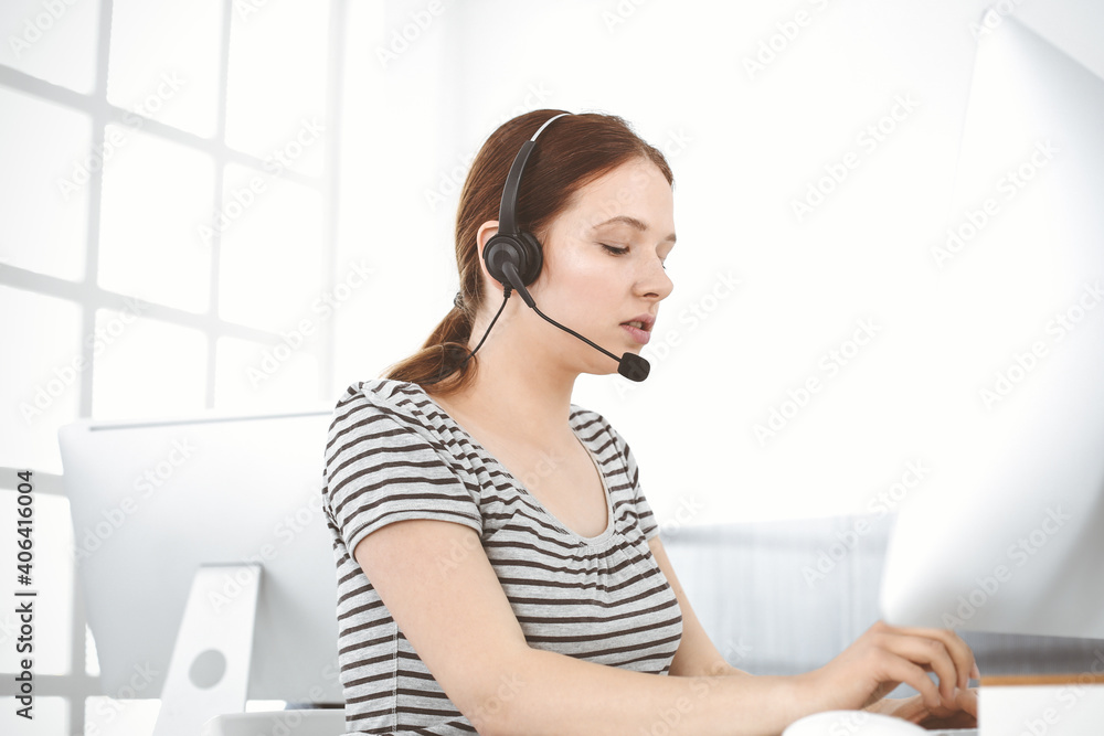 Casual dressed young woman using headset and computer while talking with customers online. Call center, business concept Casual dressed young woman using headset and computer while talking with customers online. Call center, business concept