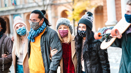 Urban milenial people walking together wearing face mask at city center - New normal lifestyle concept with multicultural friends on winter fashion clothes - Focus on middle girl with red facemask