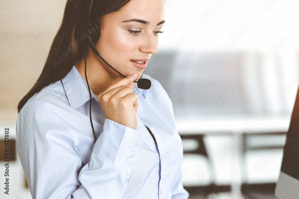Brunette female customer service representative using headset and consulting clients online. Call center Brunette female customer service representative using headset and consulting clients online. Call center