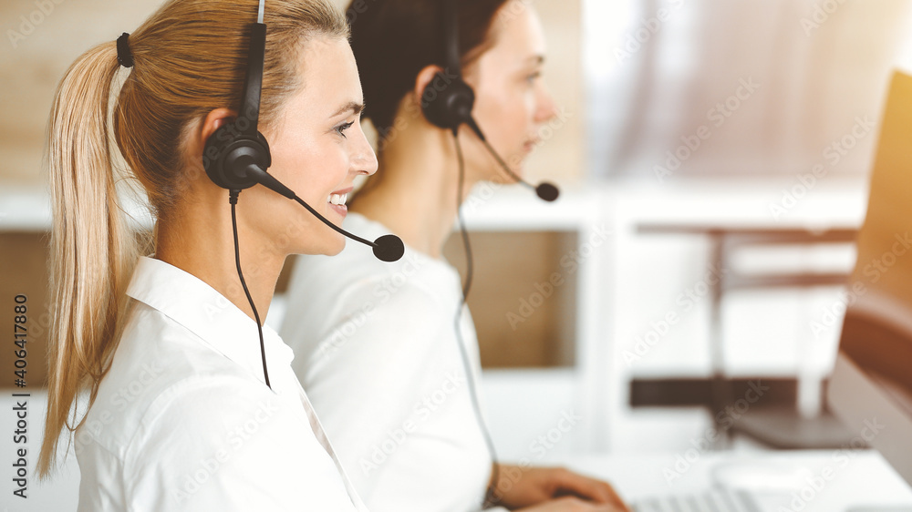 Blond female customer service representative is consulting clients online using headset in sunny office. Call center concept Blond female customer service representative is consulting clients online using headset in sunny office. Call center concept
