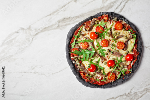 black dough pizza with anchovy arugula, capers